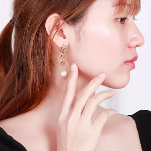 Macro detail of gold tassel earrings with geometric frames and white pearls on model