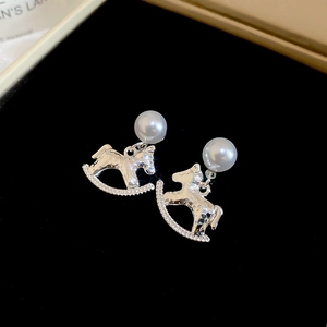 Close-up of silver rocking horse earrings with white pearls and small diamonds on velvet