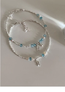 Detailed close-up of double-layer beaded bracelet with silver fish pendants and blue crystals