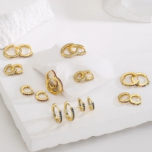 Minimalist gold hoop earrings with multi-colored gemstones on a textured stone display