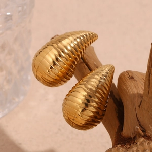 Macro detail of 18K gold plated teardrop earrings with spiral texture on wood base