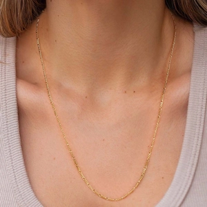 Detail of 1.7mm gold Figaro chain necklace worn by a model on a neutral background