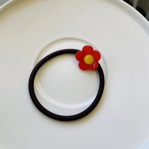 Détail d'un élastique à cheveux noir avec des breloques fleurs en résine rouge et jaune