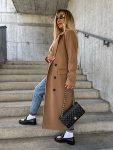 Outdoor shot of a long camel wool coat featuring a double-breasted design and notched lapels