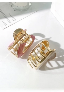 Detail view of two medium gold shark hair clips with pink and beige enamel finish