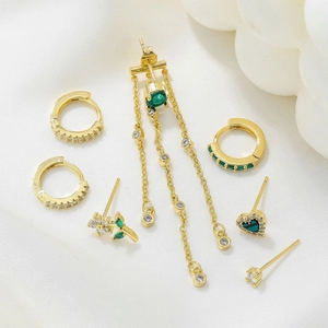 Detail view of gold earring set with green gems and zircons on white silk background