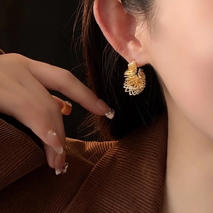 Macro detail of gold-plated twisted C-shaped earrings showing elegant spiral metal texture