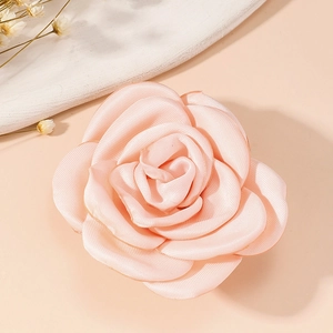 Close-up of a pink vintage fabric rose brooch with soft texture on a beige background