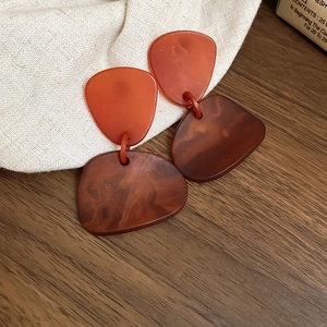 Detailed close-up of amber acrylic geometric earrings on a warm wooden surface