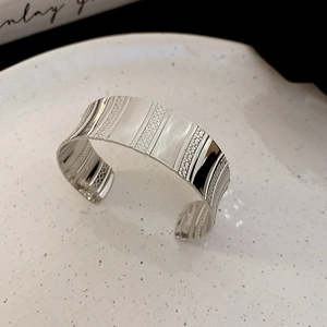 Detail view of silver open cuff bracelet with geometric striped texture on a white tray