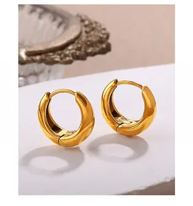 Close-up of chunky gold hoop earrings with a mirror-polished finish on stone surface