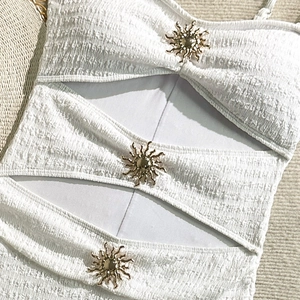 Detail of white seersucker swimsuit with hollow cut-outs and golden sun metal accents