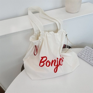 Close-up of white canvas tote bag with red Bonjour text and drawstring closure