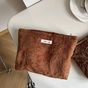 Close-up of dark brown velvet cosmetic bag with floral embroidery and simple wish label