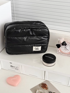 Close-up of black quilted rectangular cosmetic bag with zipper and Soda Blue brand label
