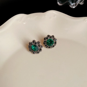 Macro view of vintage silver flower earrings with emerald stones on ceramic tray