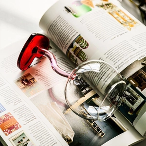 Elegant wine glass with a unique pink heart-shaped stem on an open magazine over a wooden table