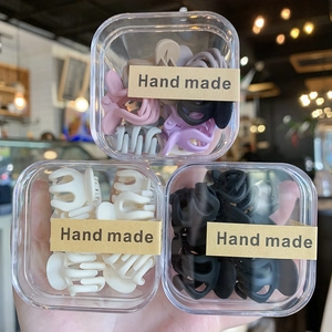 Detalle de tres cajas de mini pinzas para el cabello en varios colores con etiquetas
