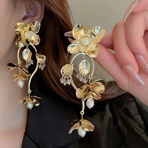 Golden floral tassel earrings with pearls and beads shown on a model's ear