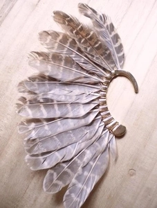 Detail view of vintage peacock feather ear cuff with golden base on wood background