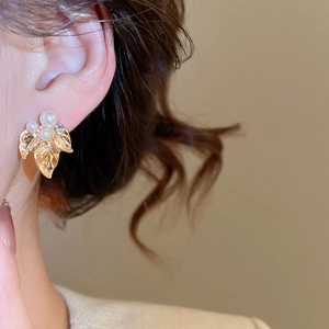 Gros plan de boucles d'oreilles feuilles dorées avec perles blanches et fini texturé