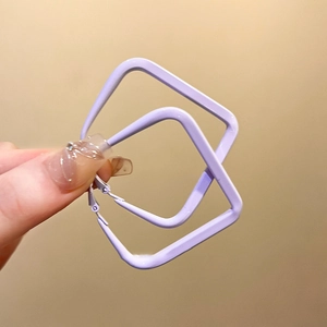 Detail view of purple square metal hoop earrings held by hand against a warm background
