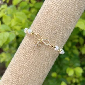 Macro detail of 18K gold bow charm with pavé crystals on a white pearl bracelet