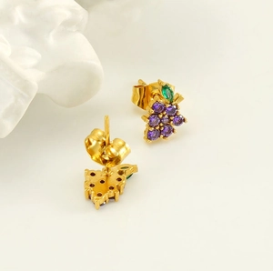Detail of gold grape earrings with purple and green zircon stones on white stone