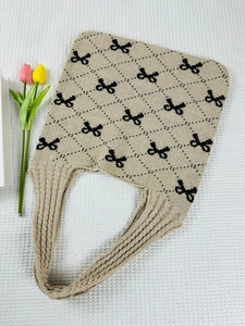 Detail of beige knit tote bag featuring black bow patterns and diamond weave texture