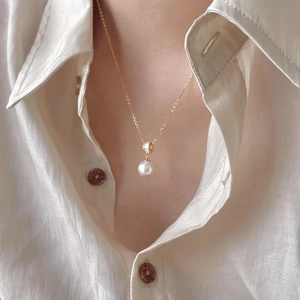 Close-up of a delicate gold chain necklace featuring a white pearl pendant and zircon stones