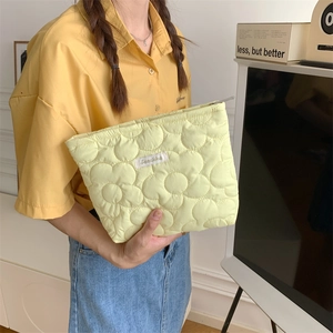 Close-up of quilted floral cosmetic bag in pale yellow with a woven logo tag