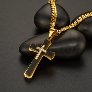 Detail of gold multilayer cross pendant with zircon stones on dark pebbles