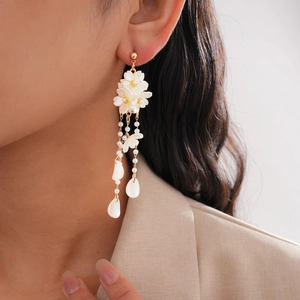 Elegant gold tassel earrings with white flowers and pearls worn by a fashion model