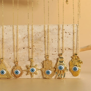 Gold Evil Eye necklaces with Hamsa Hand and heart pendants on beige travertine background