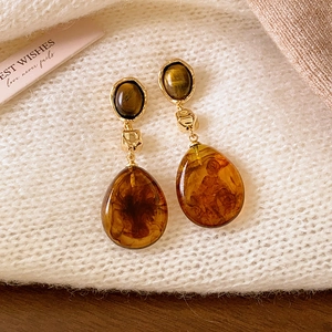 Boucles d'oreilles ovales dorées en résine ambre sur fond de tissu blanc doux