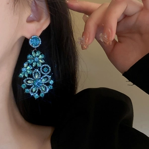 Detail shot of a model wearing large blue floral crystal drop earrings with silver pins