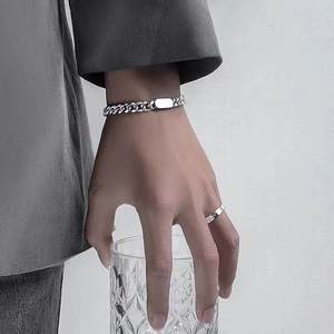 Detail of silver Cuban link bracelet with rectangle plate and ring on wrist