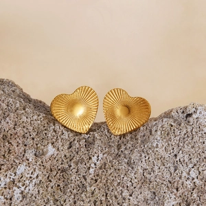 Golden heart-shaped stud earrings with radial texture displayed on a grey rock background