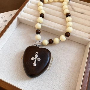 Détail du pendentif cœur en bois avec croix argentée sur un collier de perles ethnique