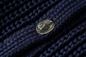 Vue macro d'un bouton métallique doré sur la texture d'un pull en maille bleu marine