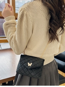 Detail of black quilted crossbody bag with white butterfly buckle and gold chain