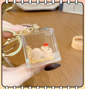 Close-up of square liquid sand keychain with a sleeping capybara and golden glitters