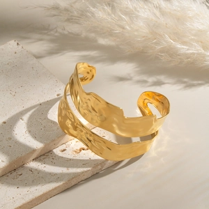 Detail of gold chunky double-layer wavy cuff bracelet with hammered texture on marble