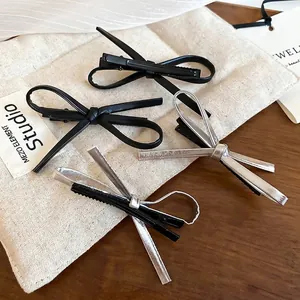 Y2K glossy faux leather bow hair clips in black and silver on a minimalist background