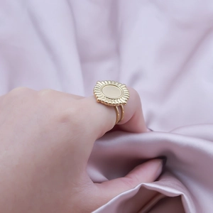 Detailed close-up of golden sunburst ring with double band on pink silk background
