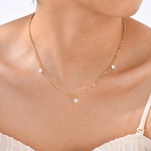 Close-up of gold titanium necklace with three clear zircon charms worn by a model