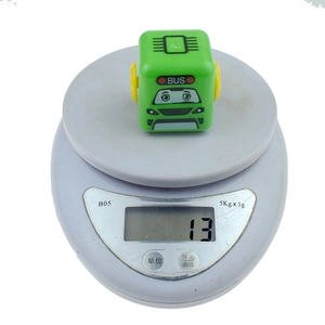 Close-up of a square green cartoon toy bus on a scale showing 13g product weight