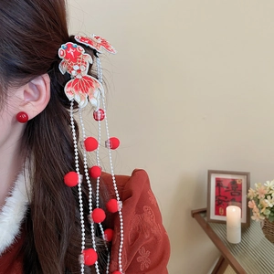 Detail showing embroidered koi flower hair clip with pearl tassels and red plush balls