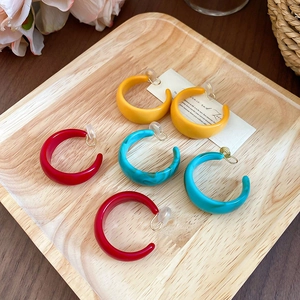 Macro shot of colorful acrylic C-shape clip-on earrings in a wooden tray