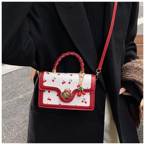 Détail du motif cerises rouges sur sac à main blanc avec fermoir floral doré élégant